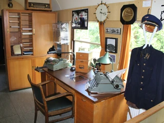 Museumslok Ausstellung Ein historisches Lokomotivbüro mit antikem Mobiliar, Schreibmaschine und Uniform auf einem Kleiderständer.