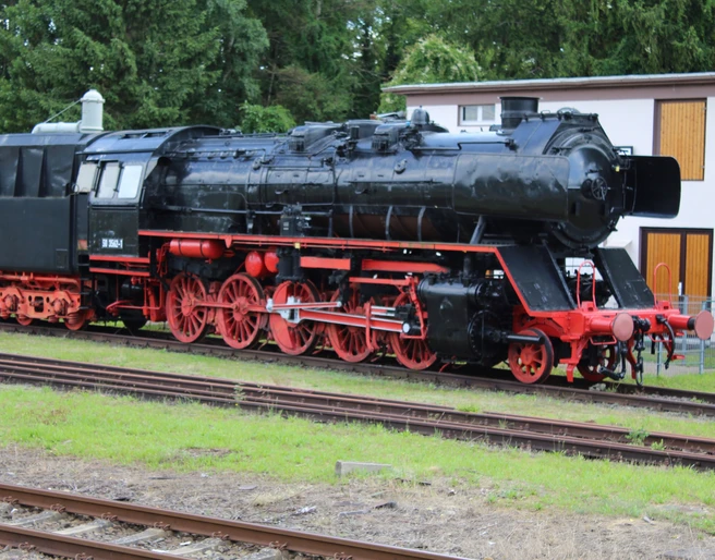 Weyhe Museumslok Historische Dampflok im Freien, schwarz mit roten Rädern, umgeben von Bäumen und einer Hütte.