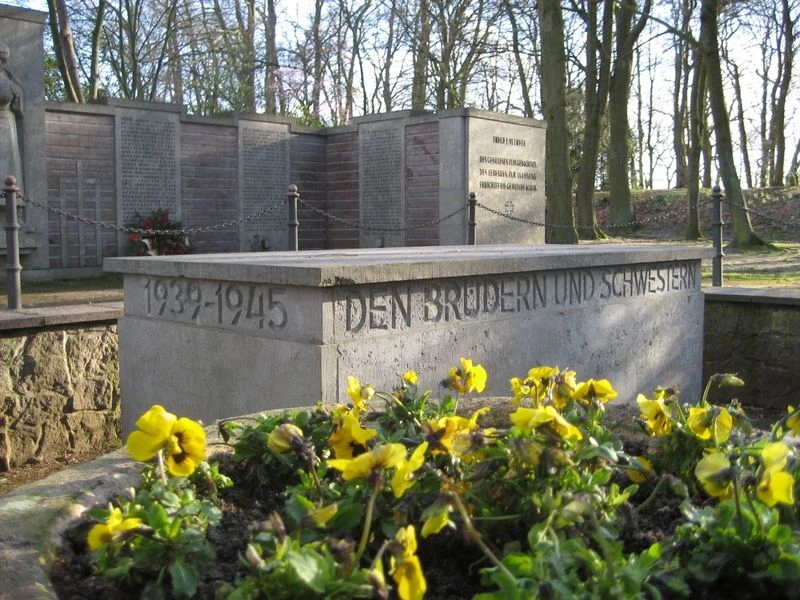 Ehrenmal Gedenkstätte mit Blumen und Inschrift "Den Brüdern und Schwestern 1939-1945", umgeben von Bäumen.