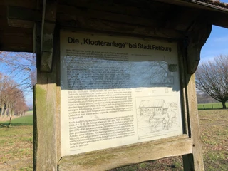 Kloster Asbeke Schild an der ehemaligen Klosteranlage; Informationstext und Zeichnung vor Landschaftskulisse.