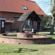 Runder, gemauerter Grillplatz mit Überdachung und Holzlager, umgeben von grüner Rasenfläche.