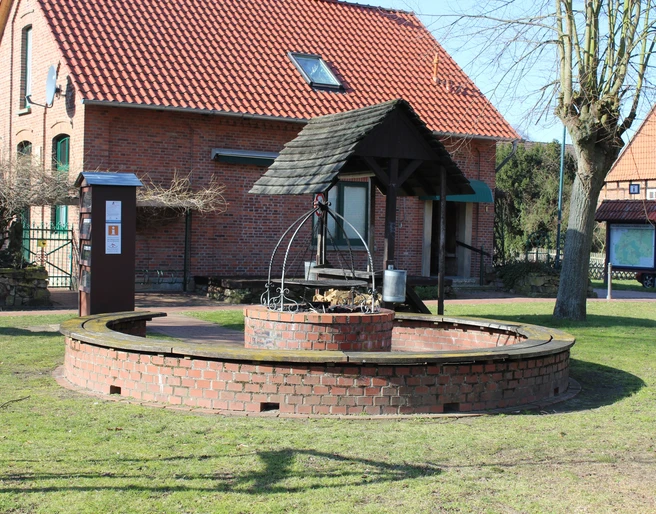 Eierbratstelle Winzlar Runder, gemauerter Grillplatz mit Überdachung und Holzlager, umgeben von grüner Rasenfläche.