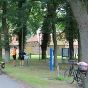 Zwei Radfahrer stehen vor historischen Fachwerkhäusern im Schafstallviertel Hülsen unter grünen Bäumen.