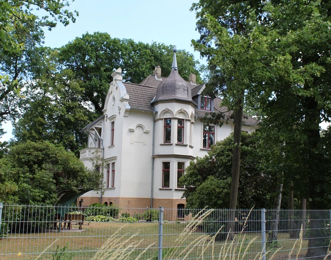 Ernst Jünger Villa Historische weiße Villa mit spitzem Turm, umgeben von Bäumen und einem gepflegten Garten.