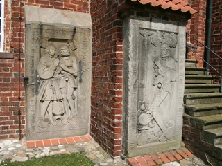 Ev.-luth. Johannis der Täufer-Kirche Drakenburg Reliefs aus Sandstein an einer roten Backsteinmauer mit Treppe, künstlerische Darstellungen von Personen.