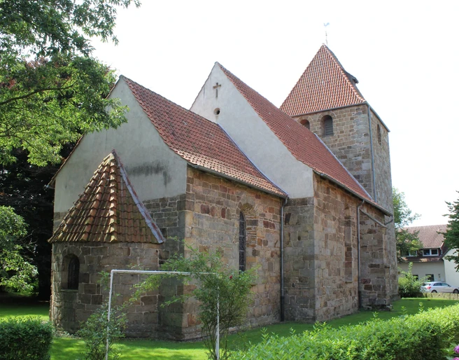 Kirche Buchholz Eine historische Steinkirche mit roten Ziegeldächern, umgeben von Bäumen und grünem Rasen.