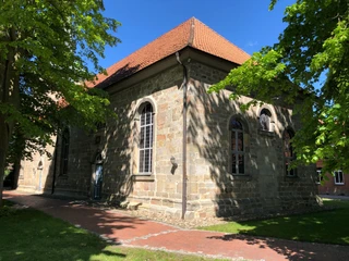 Kirche Landesbergen Historische Kirche aus Stein mit roten Ziegeldach, umgeben von Bäumen unter blauem Himmel.