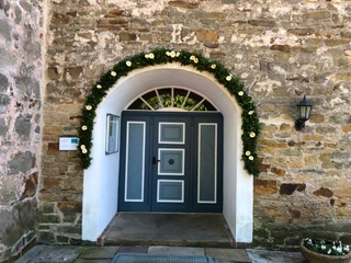 Eingangsportal aus Holz mit Blumengirlande an einem historischen Sandsteingebäude in Landesbergen.
