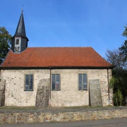 Kirche Münchehagen Historische Kirche Münchehagen mit rotem Ziegeldach und Uhrenturm, umgeben von Bäumen und Steinmauer.