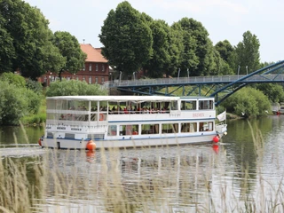 FGS Bremen an der Fußgängerbrücke Ein weißes Ausflugsschiff mit dem Namen "FGS Bremen" fährt in ruhiger Flusslandschaft unter einer Brücke.