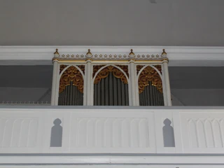 Eine kunstvoll verzierte Orgel in weißem Gehäuse mit goldenen Details, eingebaut in eine Kapelle.