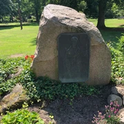 Skulptur Gedenkstein Hoppe Gedenkstein mit Bronzetafel in einer grünen Parklandschaft, umgeben von kleinen Blumenbeeten.