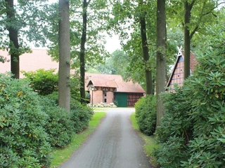 Gehannfors Hof in Warmsen Ein traditionelles Fachwerkgehöft mit Ziegeldach und grünen Toren, umgeben von üppigem Grün.