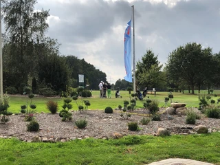 Golfplatz Rehburg-Loccum Golfer bereiten sich auf einer gepflegten Grünfläche mit umliegenden Bäumen unter blauem Himmel vor.