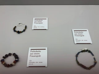 Perlenkette aus einem Frauengrab - Ausstellungsstücke im Landesmuseum Hannover Perlenketten aus Glas aus dem 8./9. Jh., ausgestellt im Landesmuseum Hannover, kreisförmig angeordnet.