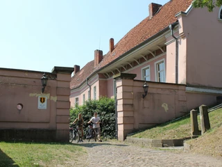 Ehemaliges Grafenschloss Hoya Altes Grafenschloss mit rötlichen Mauern und Fenstern, vor grüner Hecke und gepflastertem Weg.