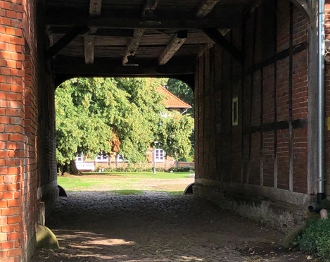 Gut Oenigstedt Thedinghausen Blick durch ein giebelgedecktes Tor auf einen gepflasterten Hof, umgeben von alten Backsteinwänden.