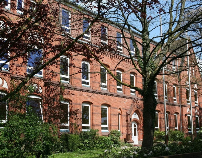 Gymnasium am Markt Schule aus roten Ziegeln mit großen Fenstern, umgeben von Bäumen und gepflegtem Grün.