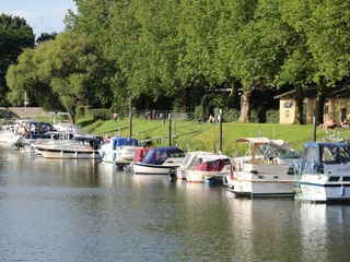 Boote im Hafen Boote im Wasser, vertäut an einem ruhigen Kai mit üppig grünem Ufer und Bäumen im Hintergrund.