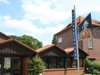 Heringsfängermuseum Heimsen Eingang Museumseingang mit modernem Schild und Flagge, flankiert von Gebäuden und grüner Vegetation.