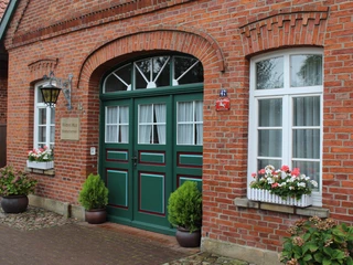 Witten Hus Liebenau Rote Backsteinfassade mit grünen Türen, dekoriert mit Blumenkästen und Pflanzen zu beiden Seiten.