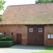 Heimatstube Wietzen Ziegelsteinbau mit Satteldach in Wietzen, Eingang mit Doppeltür, umgeben von grüner Hecke.