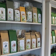 Tee-Shop Hiller Tee-Variationen in braunen und grünen Verpackungen geordnet in weißen Regalen eines Tee-Shops.
