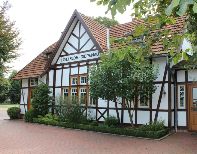 Hochzeitsbahnhof Lavelsloh Fachwerkgebäude mit gepflegtem Garten und Schildern, zeigt Hochzeitsbahnhof Lavelsloh in Niedersachsen.