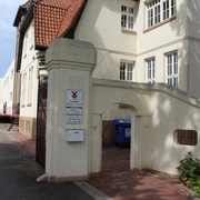 Eingang mit gemauertem Torbogen zur historischen Senffabrik Eystrup, umgeben von weißen Gebäuden.