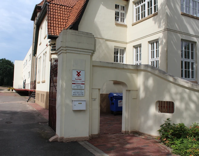 Eingang Senffabrik Eystrup Eingang mit gemauertem Torbogen zur historischen Senffabrik Eystrup, umgeben von weißen Gebäuden.