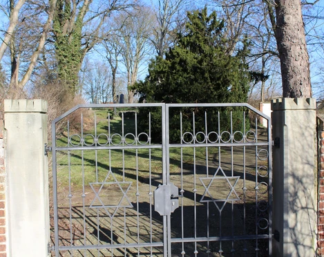 Jüdischer Friedhof Nienburg Metalltor mit Davidstern-Motiven öffnet den Zugang zu einem von Bäumen umgebenen Friedhof.