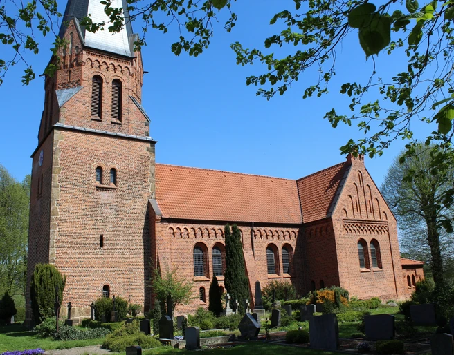 Historische Backsteinkirche mit markantem Turm und grüner Umgebung an einem klaren blauen Himmel.
