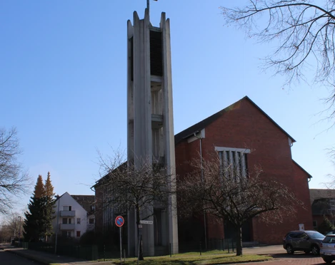 Backsteinkirche St. Bernward mit markantem Eingangsturm, umgeben von Bäumen und wolkenlosem Himmel.
