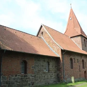 Kirche St. Cosmae et Damiani Hassel Backsteinkirche mit markantem Turm und rötlichen Dachziegeln, umgeben von grünen Bäumen und Mauerwerk.