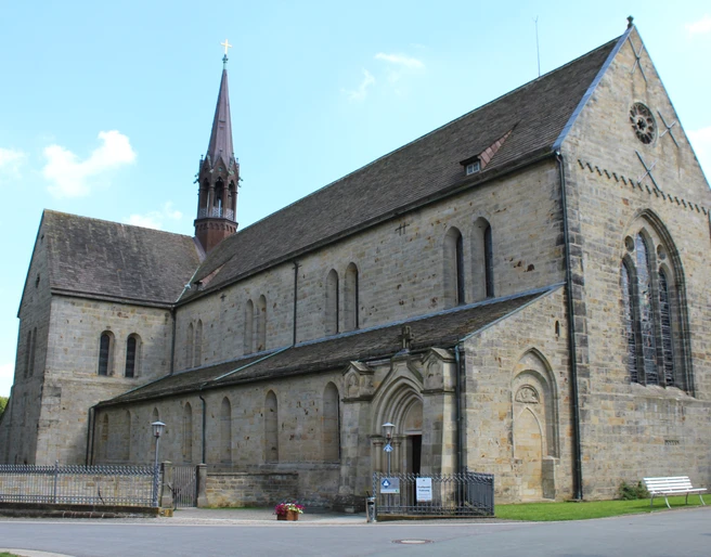 Romanische Fassade des Klosters Loccum mit hohen Fenstern und einem spitzen Turm bei klarem Himmel.