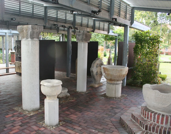 Steingefäße Lapidarium Steingefäße und Säulenreste unter einem überdachten Bereich auf gepflastertem Boden bei Tageslicht.