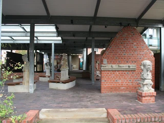 Lapidarium seitlich Ein überdachter Bereich mit Ziegelmauern und Skulpturen. Metallträger stützen die Holzkonstruktion.