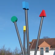 Logo-Stelen Vier unterschiedlich gefärbte, senkrechte Metallstangen als modernes Kunstwerk unter klarem Himmel.
