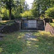 Ruinen einer historischen Steinmauer inmitten eines lichten Waldes an einem sonnigen Tag.