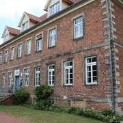 Historisches Backsteingebäude mit weißen Sprossenfenstern und Treppe, umgeben von Grünflächen.