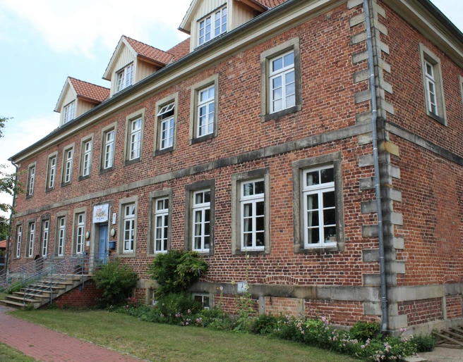 Mehrgenerationenhaus Historisches Backsteingebäude mit weißen Sprossenfenstern und Treppe, umgeben von Grünflächen.