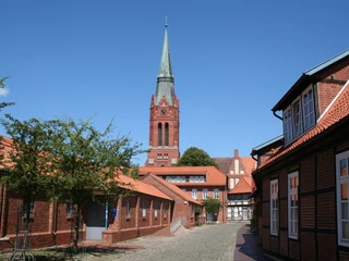 Kirchturm von St. Martin in Nienburg überragt umgebende Backsteingebäude, blauer Himmel im Hintergrund.