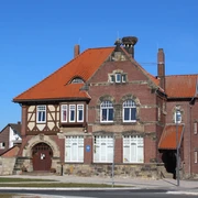 Stadt Rehburg-Loccum Polizei Backsteingebäude mit roten Ziegeldächern, großen Fenstern und einem Storchennest auf dem Schornstein.