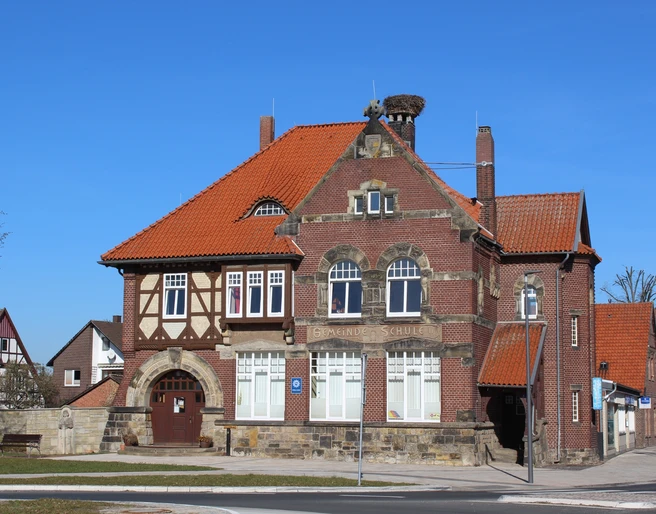 Stadt Rehburg-Loccum Polizei Backsteingebäude mit roten Ziegeldächern, großen Fenstern und einem Storchennest auf dem Schornstein.
