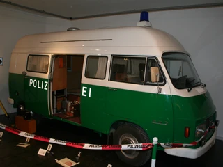 Polizeibus im Polizeimuseum Ein grüner Polizei-Van im Museum, mit offener Tür und Ausstellungsstücken um ihn herum.
