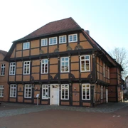 Fachwerkhaus mit rotem Ziegeldach und weißen Fensterrahmen, umgeben von gepflasterten Wegen.