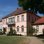 Quaet-Faslem-Haus Historisches Herrenhaus in Pastellrosé mit großen Fenstern, umgeben von gepflegten Gartenanlagen.
