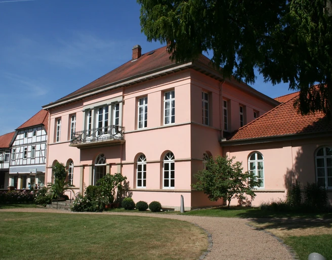 Quaet-Faslem-Haus Historisches Herrenhaus in Pastellrosé mit großen Fenstern, umgeben von gepflegten Gartenanlagen.