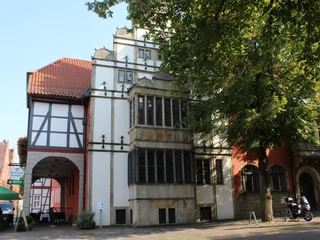 Rathausgiebel Historischer Rathausgiebel mit Fachwerkanbau bei Sonnenschein, flankiert von Bäumen und Bürgersteig.
