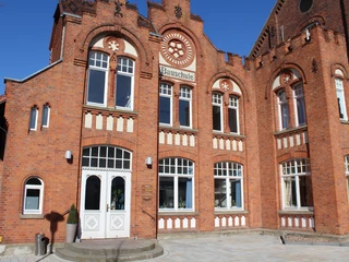 Bauschule Rehburg Historisches Backsteingebäude mit großen Fenstern, geschwungenen Verzierungen und einem zentralen Eingang.